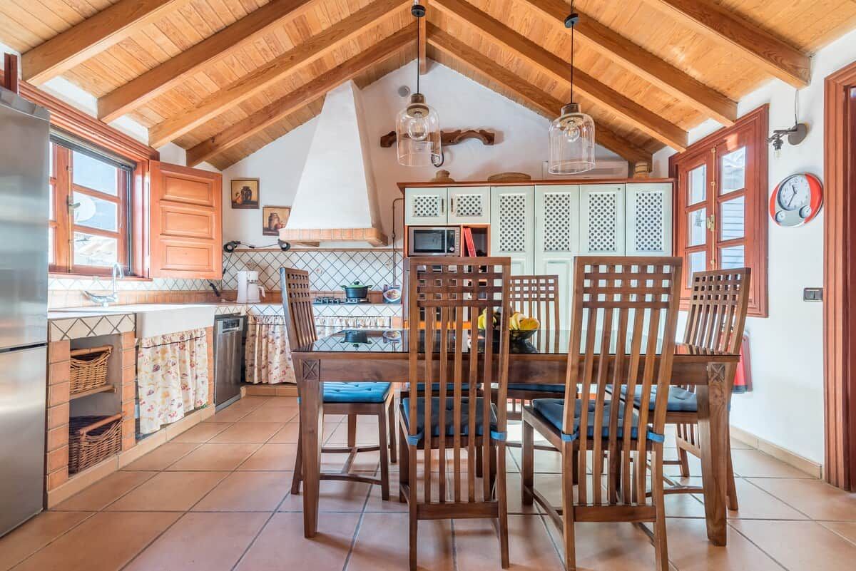 Une cuisine avec des poutres en bois, une table à manger avec des chaises et une horloge au mur.
