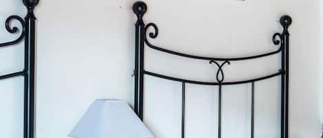 Une chambre à coucher avec un lit en métal, une table de chevet avec une lampe, deux tableaux encadrés au mur et un coussin vert sur le lit.