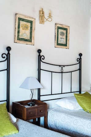A bedroom with a metal bed frame, a bedside table with a lamp, two framed pictures on the wall, and a green pillow on the bed.