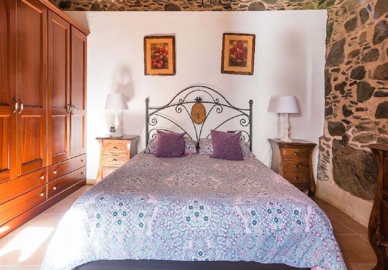 Ein Schlafzimmer mit einem Bett, zwei Nachttischen, einem Holzschrank und einer Steinwand.