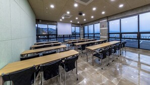 A classroom with tables and chairs, large windows with a view of a body of water and hills, and a ceiling with recessed lighting. - Aria Pension Resort (Yeosu)