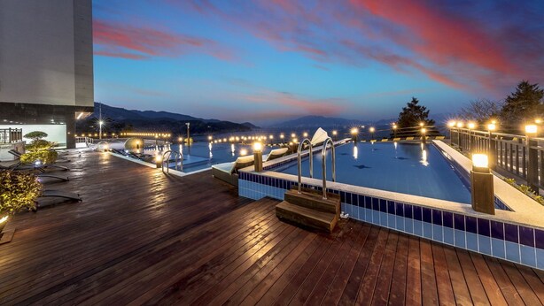 A rooftop pool area with a wooden deck, multiple pools, and surrounding lights. - Aria Pension Resort (Yeosu)