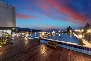 A rooftop pool area with a wooden deck, multiple pools, and surrounding lights. - Aria Pension Resort (Yeosu)