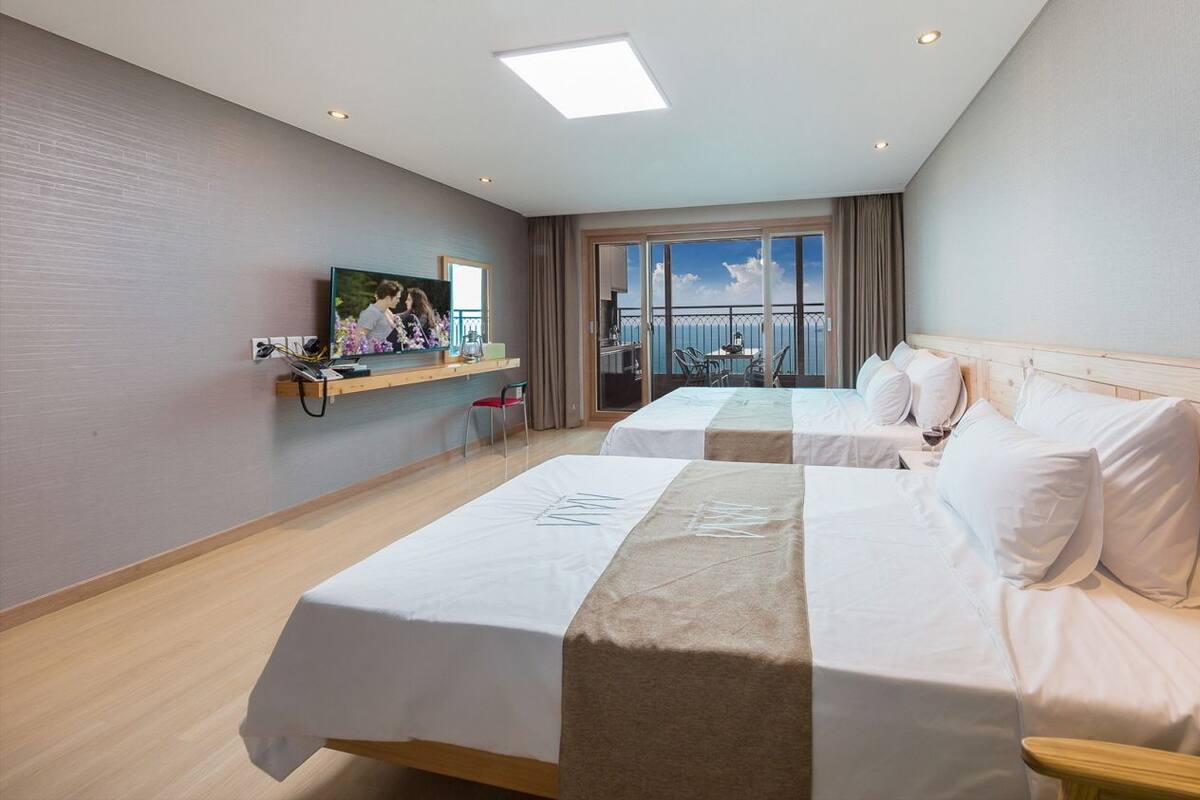 A hotel room with two beds, a TV, a balcony with a view, and a wooden headboard.