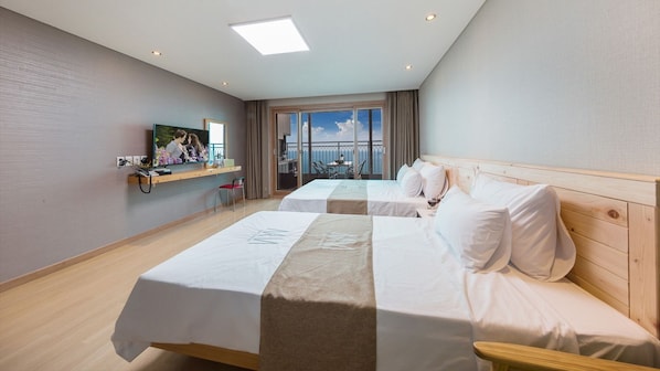 Habitación de hotel con dos camas, televisión, balcón con vistas y cabecero de madera.