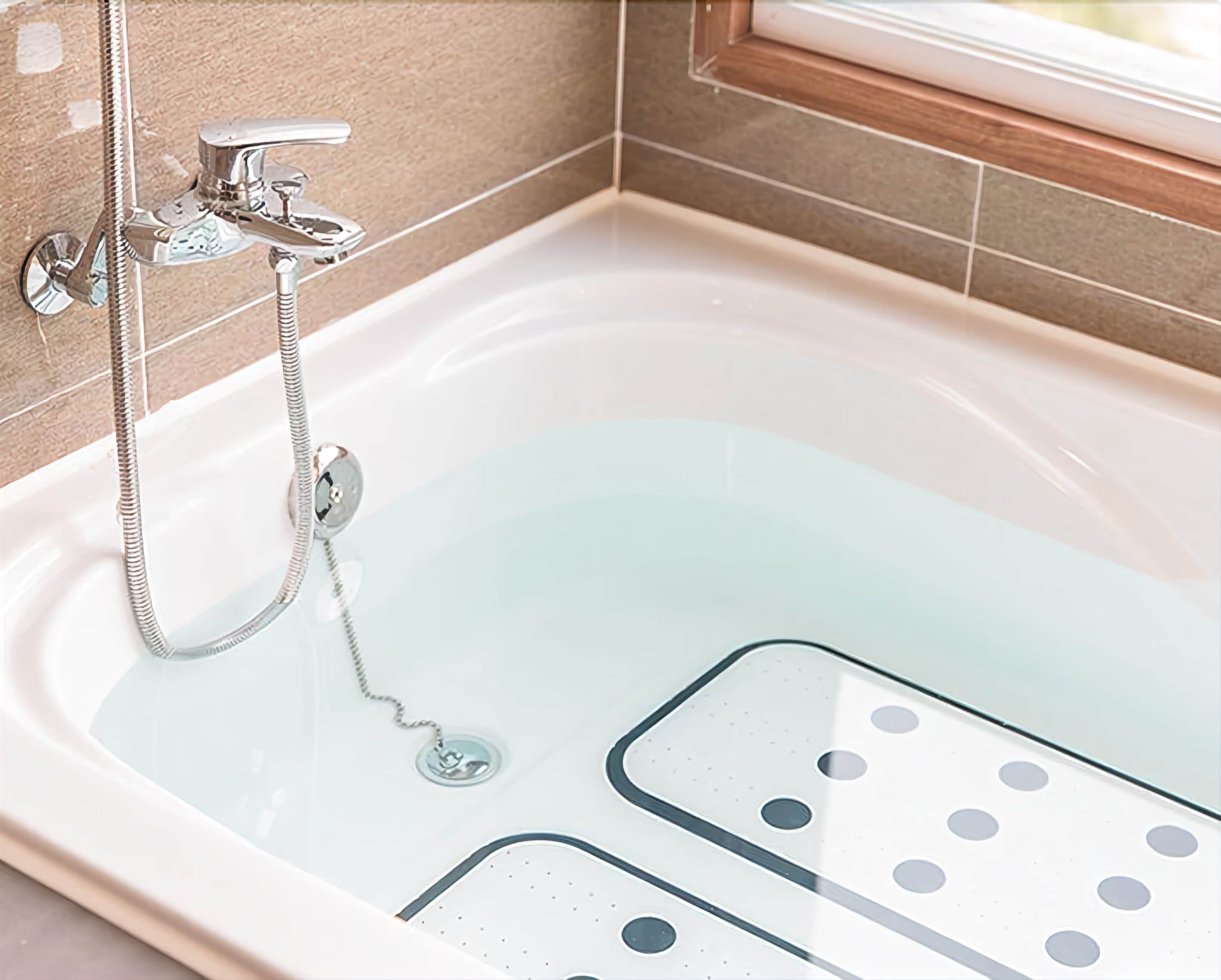 A modern bathtub with a handheld showerhead and a built-in seat.