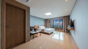 A hotel room with a large bed, a desk, a chair, a TV, and a balcony with a view. - Aria Pension Resort (Yeosu)