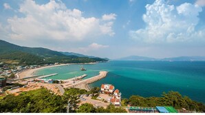 A coastal town with a beach, a pier, and a mountainous backdrop. - Aria Pension Resort (Yeosu)