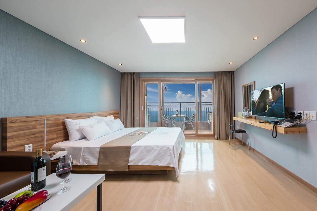 A hotel room with a bed, a desk with a computer, a TV, and a balcony with a view.