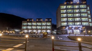 A multi-story hotel with a well-lit facade, outdoor seating area, and a visible entrance to the Aria Pension Resort. - Aria Pension Resort (Yeosu)