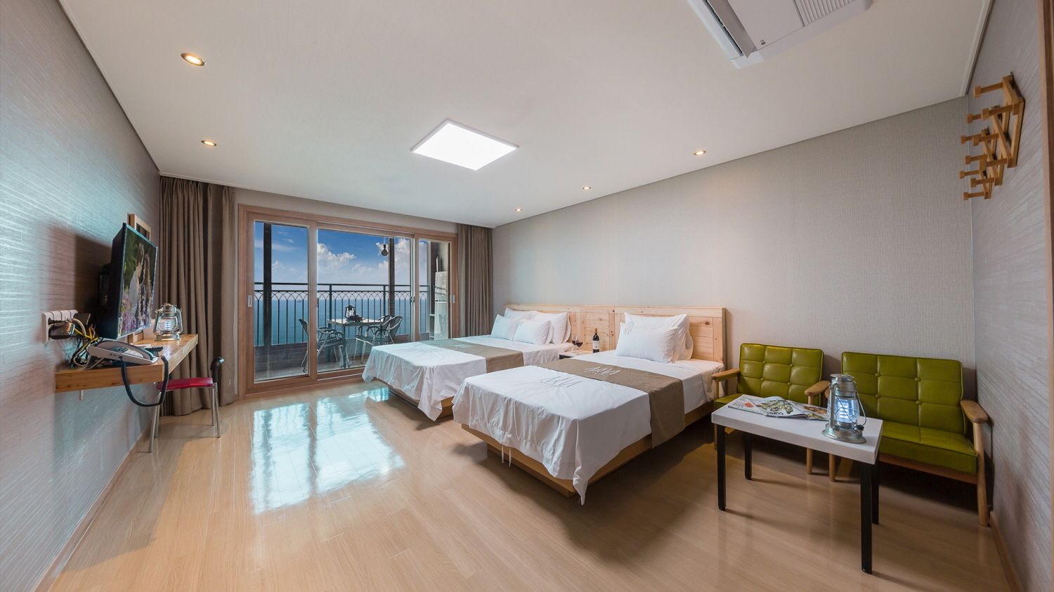 Een hotelkamer met twee bedden, een balkon, een bureau en een groene sofa.
