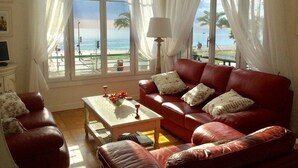 A living room with a red leather sofa, a white coffee table, and a view of the beach through large windows. - STUNNING BEACHFRONT APARTMENT ON PROMENADE,  ENDLESS SEAVIEWS, SUPERB LOCATION  (Nice)