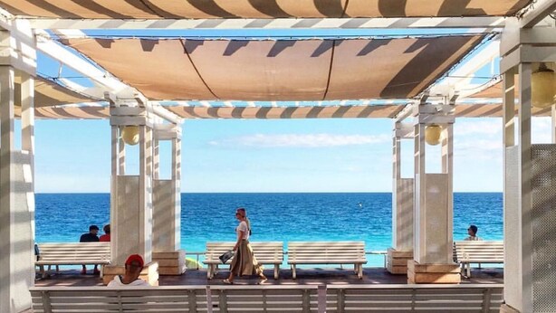 An outdoor seating area with a view of the ocean, featuring a pergola with striped awnings and wooden benches. - STUNNING BEACHFRONT APARTMENT ON PROMENADE,  ENDLESS SEAVIEWS, SUPERB LOCATION  (Nice)