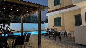 Uma área de piscina ao ar livre com pergolado, espreguiçadeiras e uma mesa.