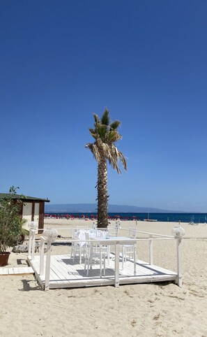 A beachside setup with a palm tree, white outdoor furniture, and a wooden deck. - Private gated Villa sleeps 12. Large pool & garden, AC ,WiFi close to the beach. (Isca Marina)