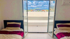 Quarto com duas camas, porta de correr de vidro que dá para área externa e vista de um edifício com telhado verde.