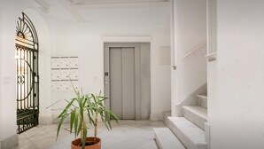 Ein heller, moderner Korridor mit einer Topfpflanze, einem Metallgitter, einer Tür und einer Treppe.