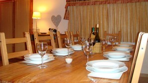 A dining table set with plates, glasses, and a bottle of wine, with chairs around it.