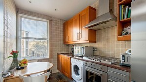 A compact kitchen with wooden cabinets, a built-in washing machine, a stove, and a refrigerator. - Homely - in the heart of Camden (London)
