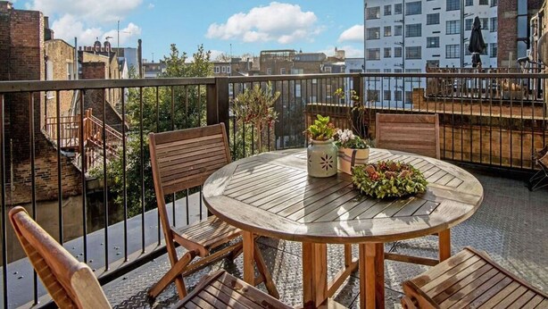 A round wooden table with four chairs on a balcony, surrounded by a metal railing. There are potted plants on the table. - Homely - in the heart of Camden (London)