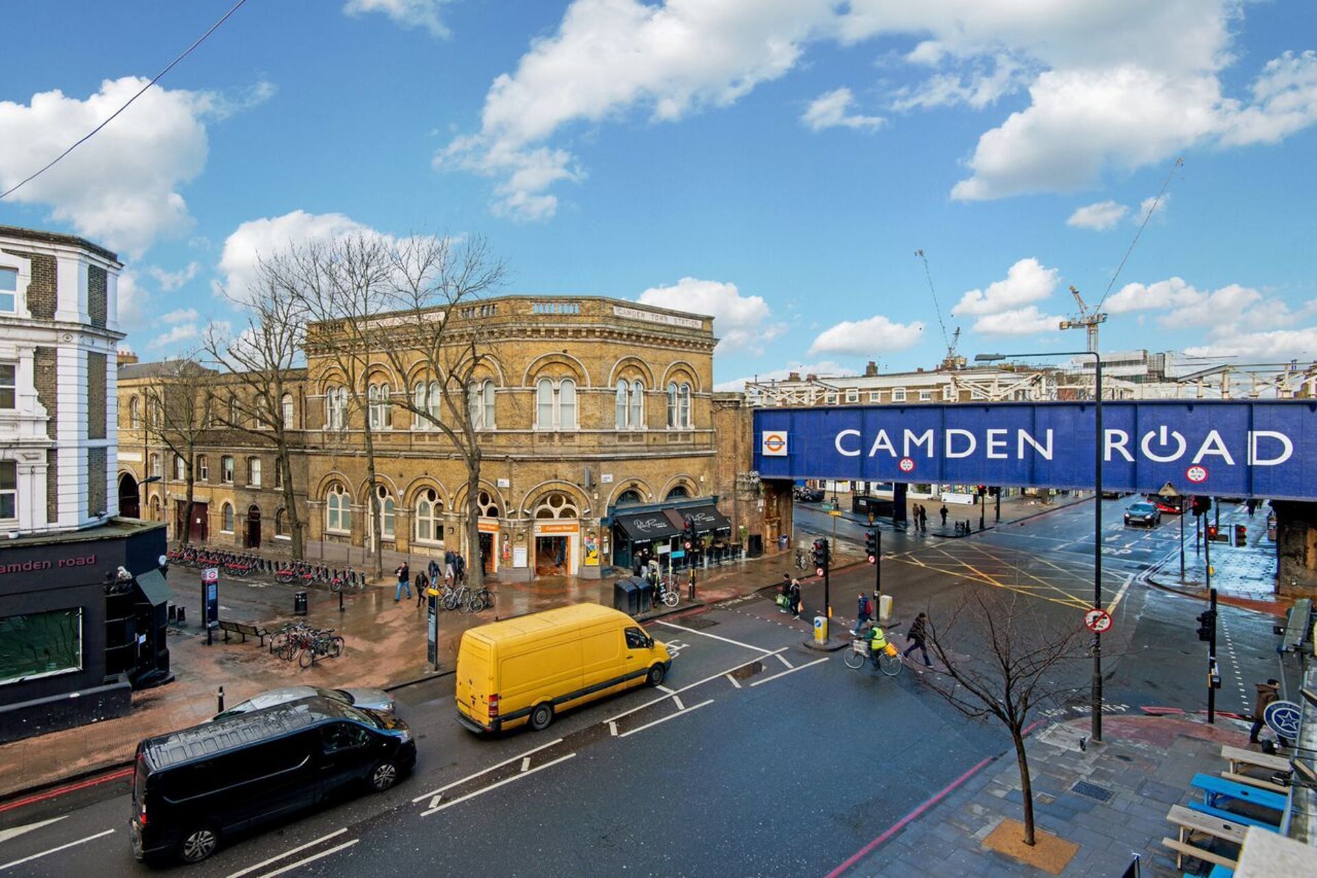 A street view with a historic building, a yellow van, and a blue sign for Camden Road.