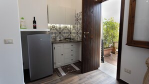 Una cocina compacta con refrigerador, un lavamanos y una puerta de madera que da a un balcón.