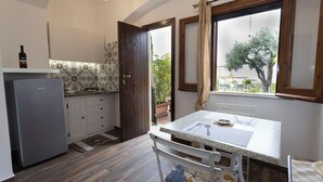 Cocina compacta con refrigerador, una mesa de comedor con camino de mesa y una ventana con cortinas.