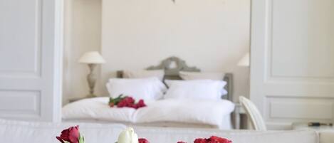 A bedroom with a bed, a chandelier, and a vase of roses in the foreground.
