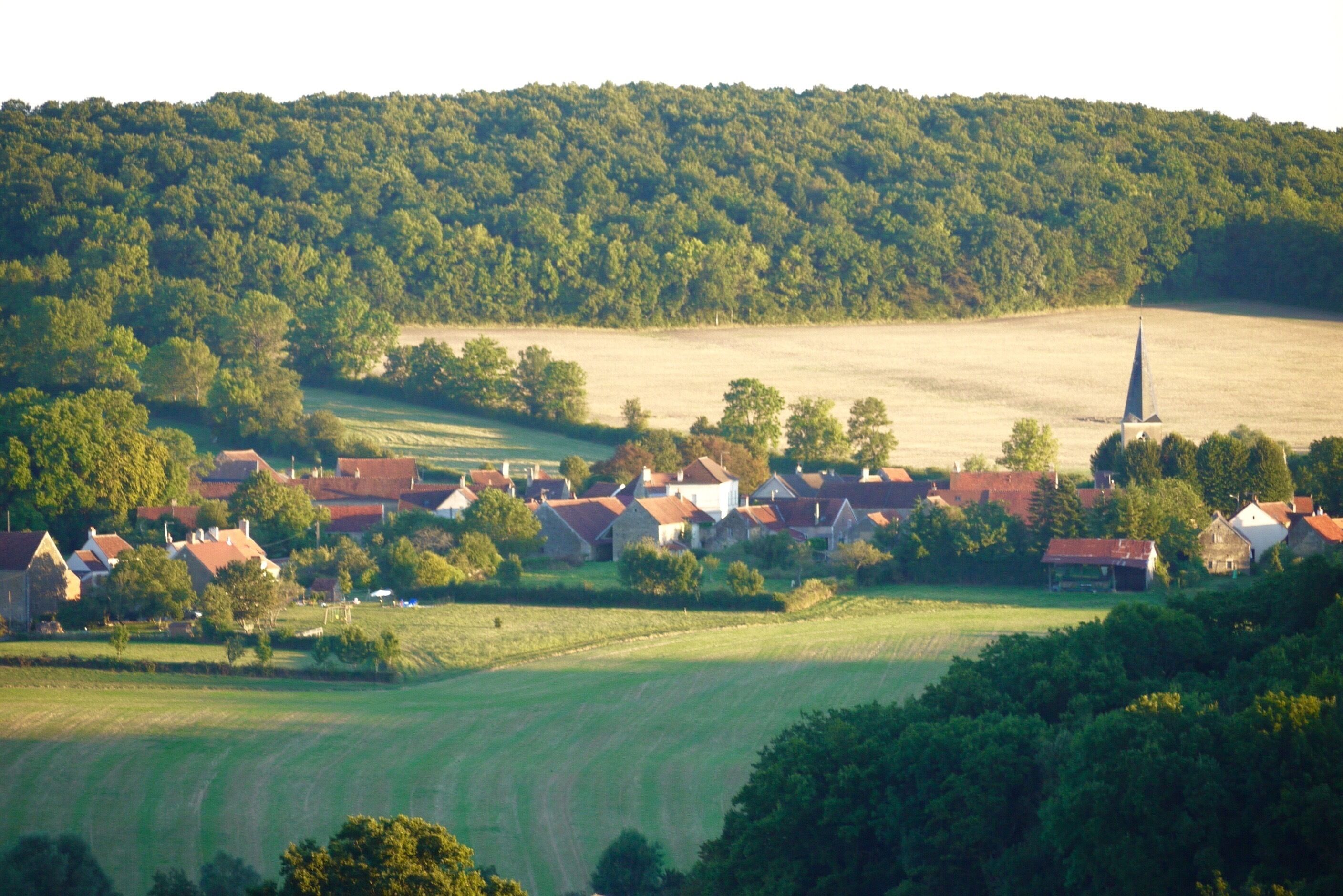 Uma aldeia rural com casas, uma igreja e campos ao redor.