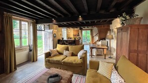 A cozy living room with a sofa, a coffee table, and a staircase leading to a kitchen. - Cottage and private garden - rural bliss for two (or 4 with mezzanine) (Corsaint)