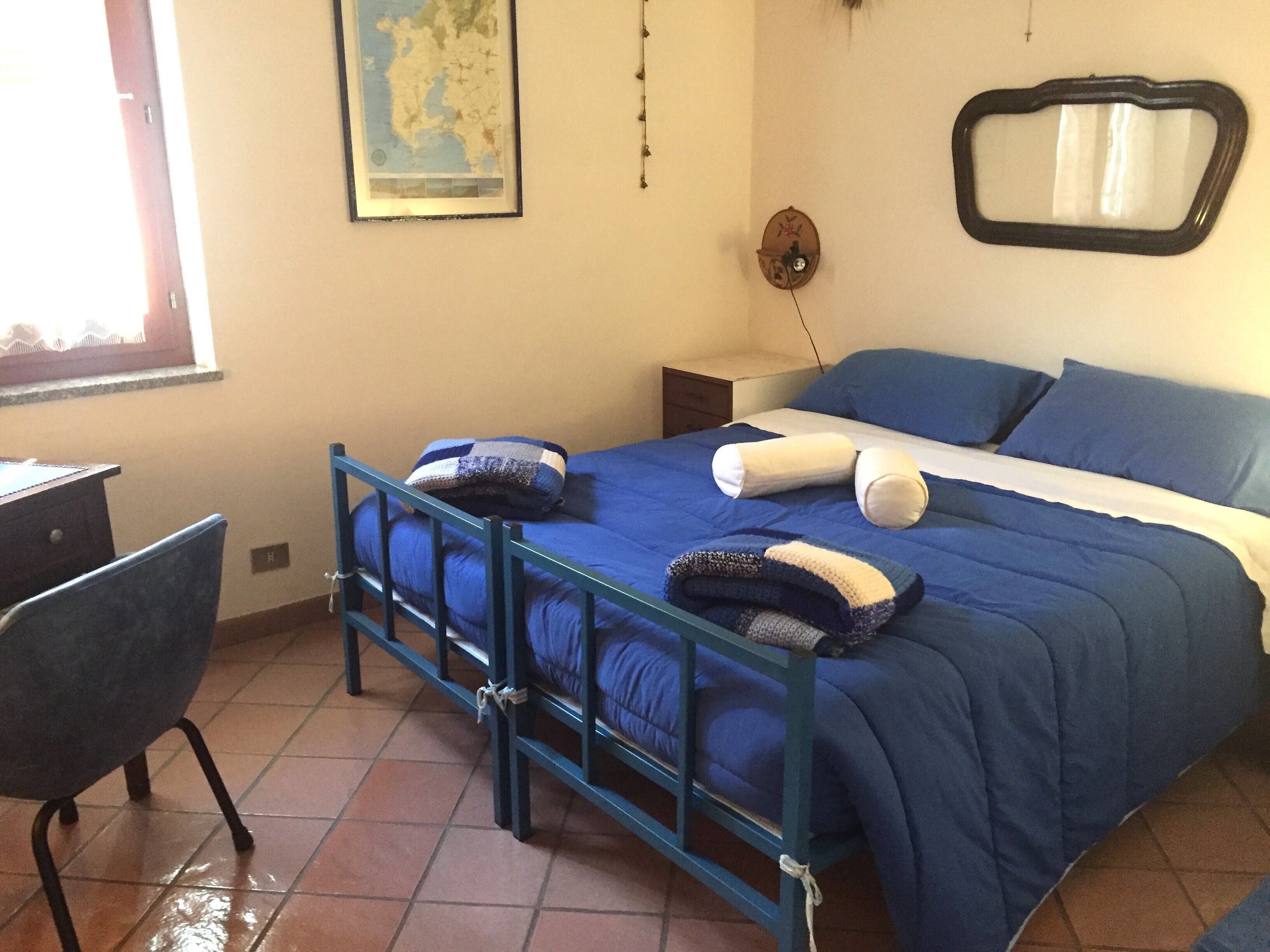 Une chambre à coucher avec un lit, une chaise, un bureau, une carte accrochée au mur et une fenêtre.