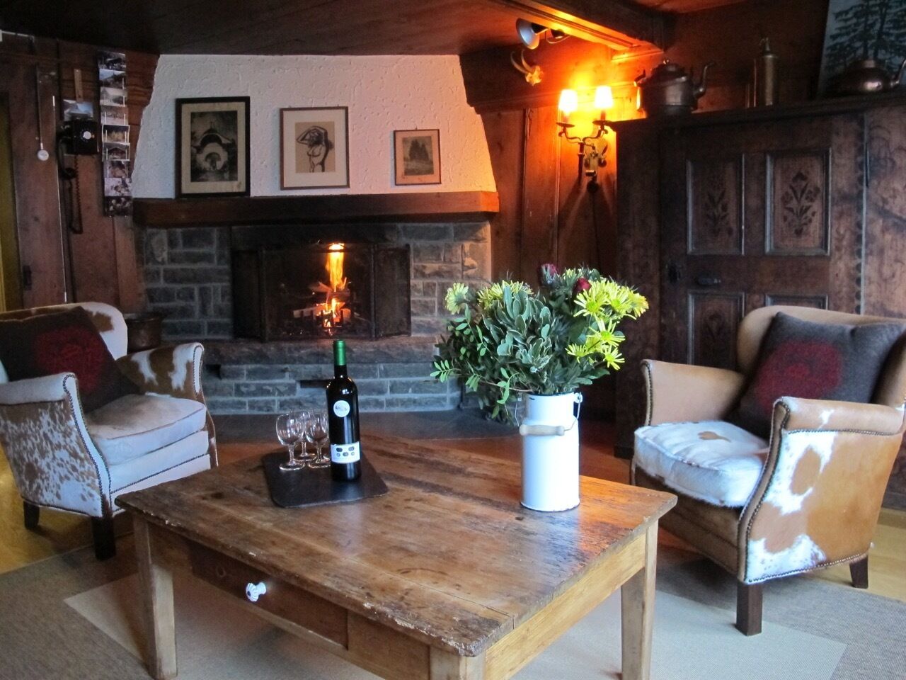 A cozy living room with a fireplace, two leather armchairs, a wooden coffee table, and a potted plant.