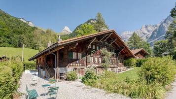 A traditional wooden chalet with a sloped roof, a stone foundation, and a gravel patio with outdoor seating.