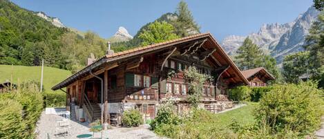 A traditional wooden chalet with a sloped roof, a stone foundation, and a gravel patio with outdoor seating.