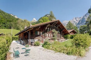 Un chalet traditionnel en bois, doté d’un toit à pente, de fondations en pierre et d’une terrasse en gravier avec des meubles d’extérieur.