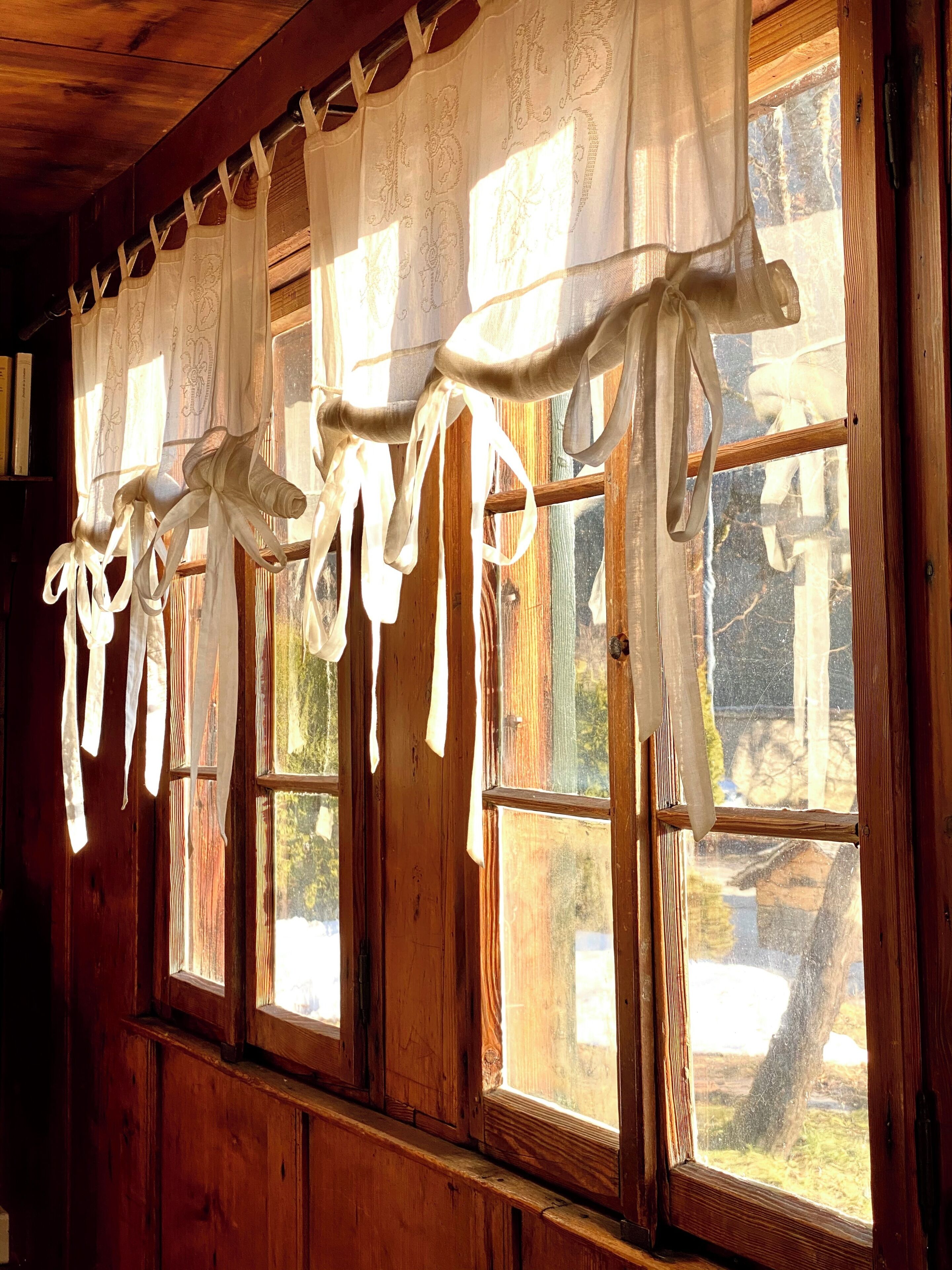 A room with wooden walls and a window with a curtain rod holding white curtains.
