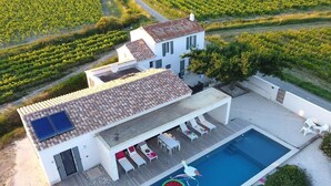 A modern villa with a swimming pool, outdoor seating, and vineyard views.
