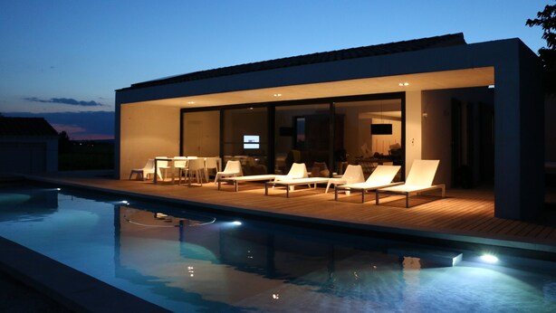 A modern house with a swimming pool, lounge chairs, and a dining area.