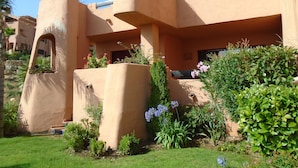 Ein modernes Gebäude mit einem einzigartigen architektonischen Design, das ein Flachdach, große Fenster und einen gepflegten Garten mit verschiedenen Pflanzen und Blumen zeigt.