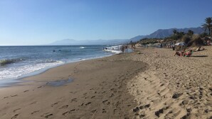 Ein Strand mit Fußabdrücken, Personen und Sonnenschirmen.
