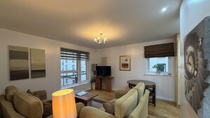 Ein Wohnzimmer mit einer Sofagarnitur, einem Couchtisch, einem Fernseher und einem Gemälde an der Wand.