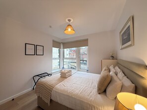 A bedroom with a bed, a bedside table, a window, and a hanging light fixture. - Holyrood Apartment with parking & lift access (Edinburgh)