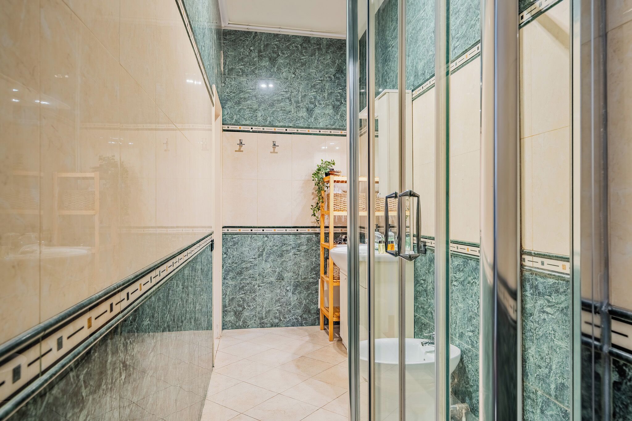 A modern bathroom with a glass shower enclosure, a wooden shelf with toiletries, and a marble-tiled floor.