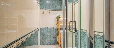 A modern bathroom with a glass shower enclosure, a wooden shelf with toiletries, and a marble-tiled floor.
