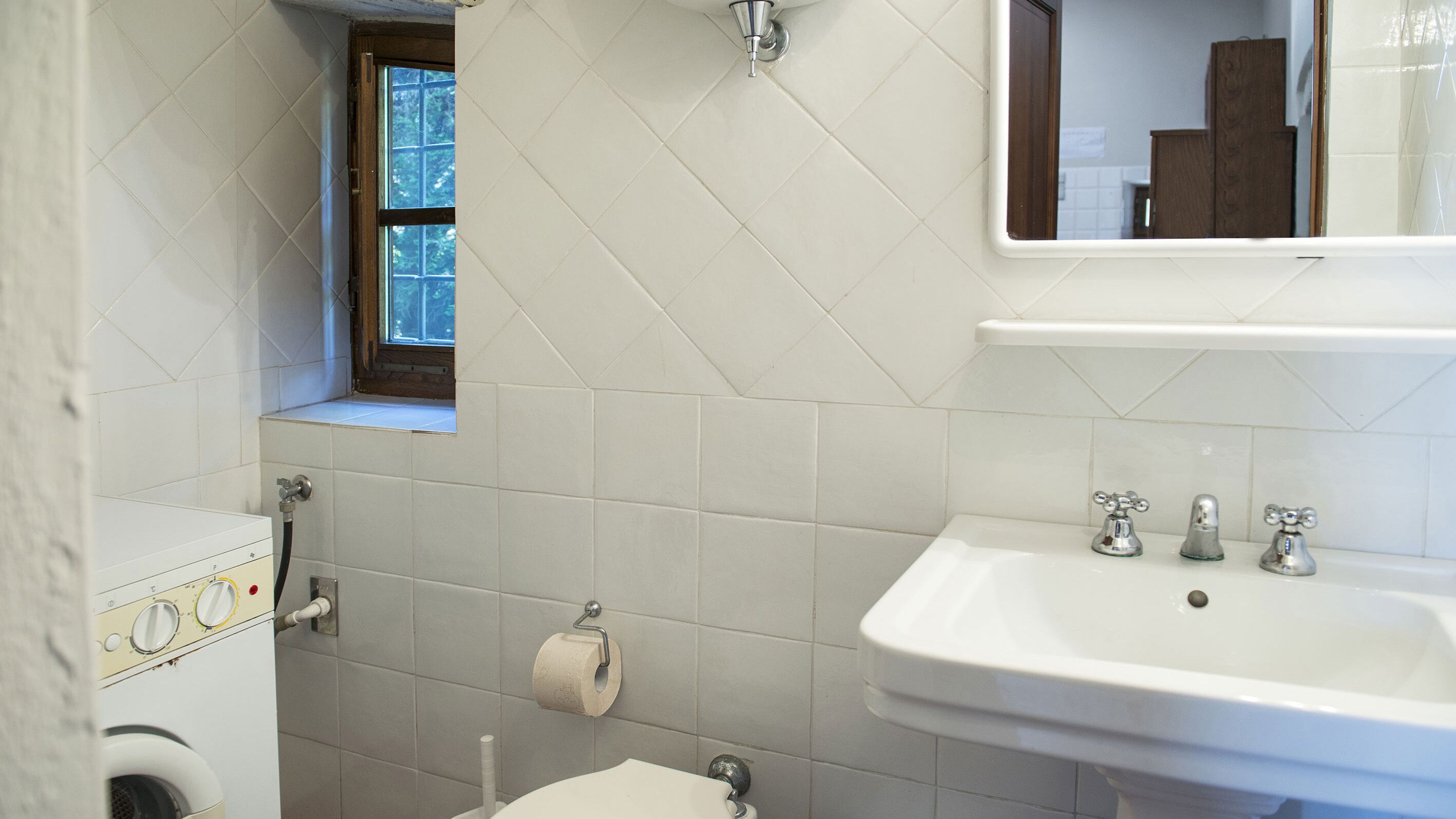 Ein Badezimmer mit Waschmaschine, Toilette, Waschbecken und einem Fenster.