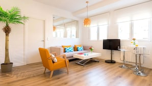 Una sala de estar moderna con sofá, sillón, mesa de centro y un comedor con taburetes de bar.