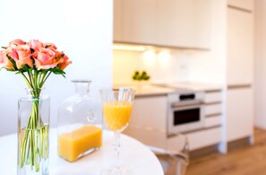 Een keuken met een wit aanrecht, een glazen vaas met bloemen, een glas sinaasappelsap en een stuk zeep.