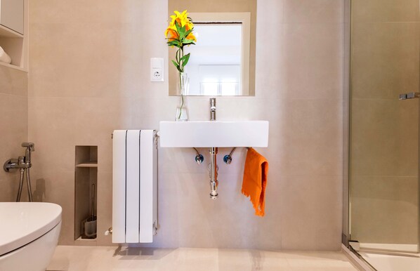 Et moderne badeværelse med en hvid vask, bruseafskærmning i glas og et toilet.