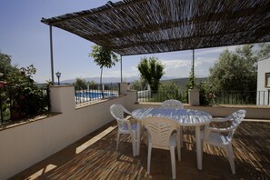 Une terrasse extérieure avec une table et des chaises, une pergola et une vue sur la mer et les collines.