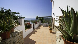 Eine Terrasse mit Steinfliesen, Blumentöpfen und einer weißen Wand.